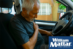 older man holding heart while driving his car